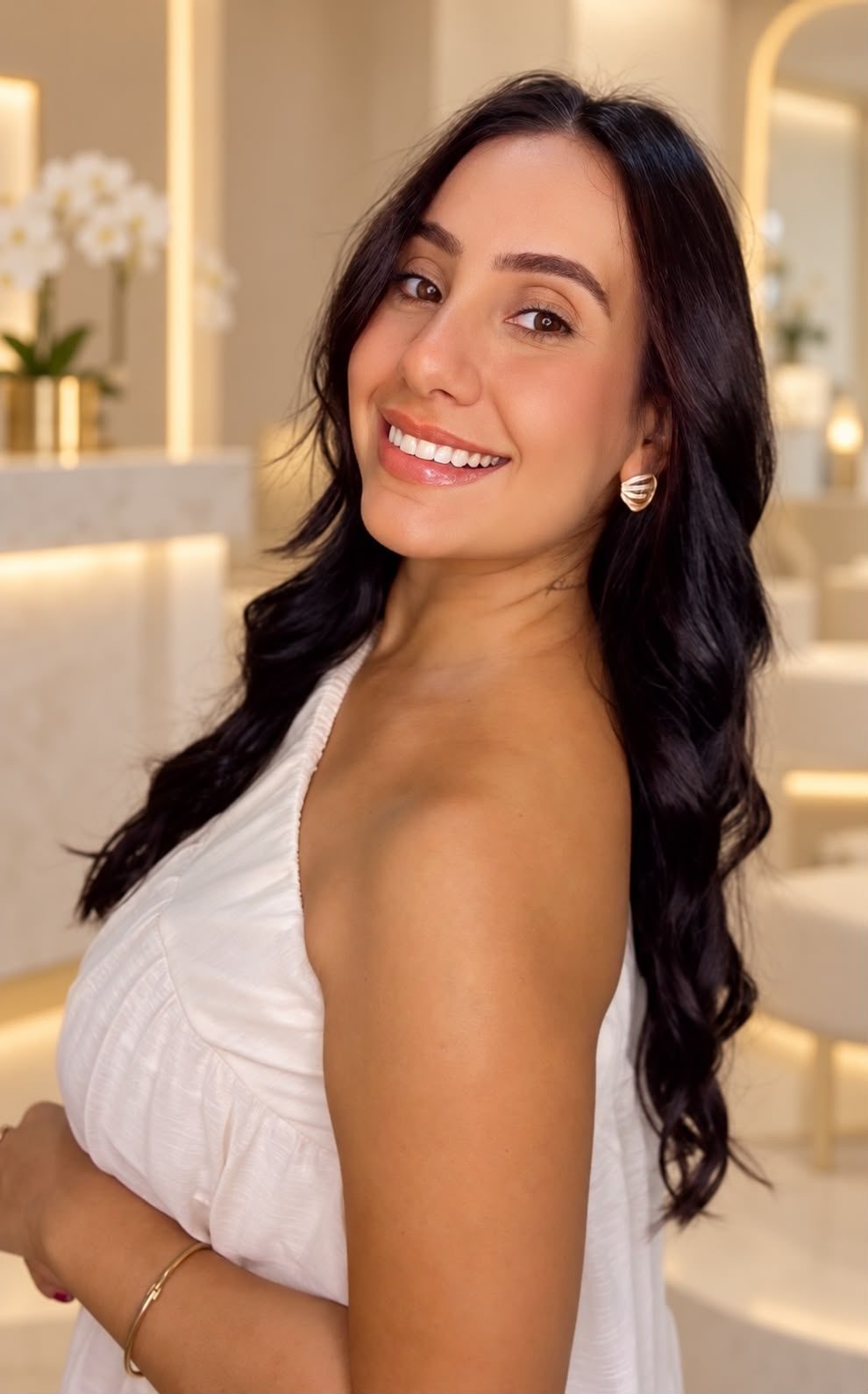 Yasmin Merlino sorrindo, de vestido branco, no espaço de atendimento